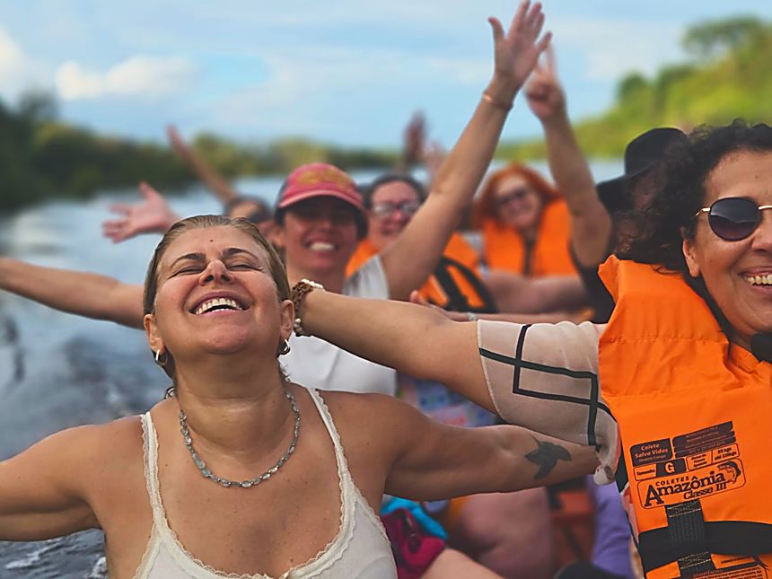 Participante de braços abertos rindo dentro do barco, no meio do rio