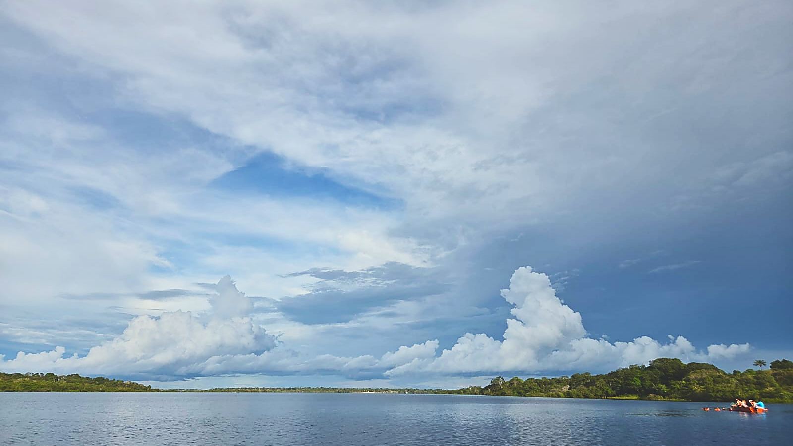 O rio Negro aberto, com a linha de mata baixa no horizonte e nuvens altas