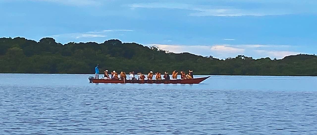 A canoa grande atravessando o rio Negro, pequena contra a linha de mata